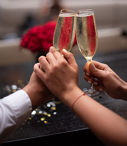 a couple holding hands and glasses of champagne with red roses in the background