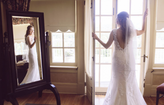 bridge in gown posing amoung open french doors while looking at reflection in the mirror