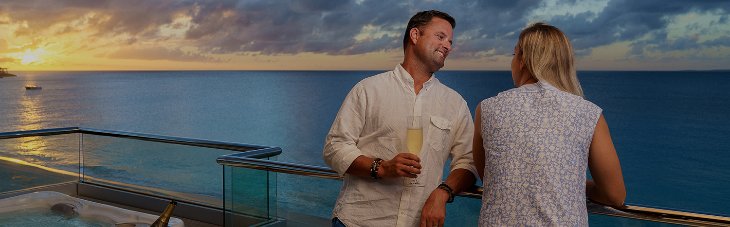 couple leaning on glass balcony overlooking ocean with champagne
