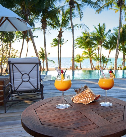 tiamo resort infinity pool overlooking beach with table set up and 2 cocktails