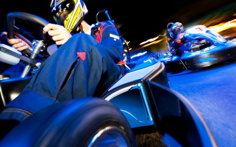a man go karting at an amusement park with a helmet on and cool blue lighting over him