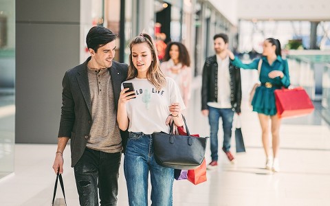 man and woman walking inside a mall looking at their phone