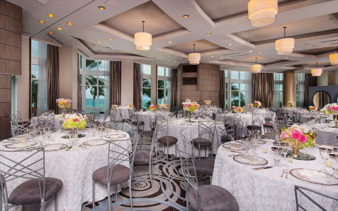 a spacious room with large windows overlooking the ocean set up for a big dinner party