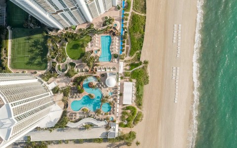 an arial eye view of a hotel with two pools on the beach
