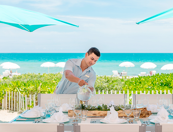 waiter pouring water into glasses by a beachside table