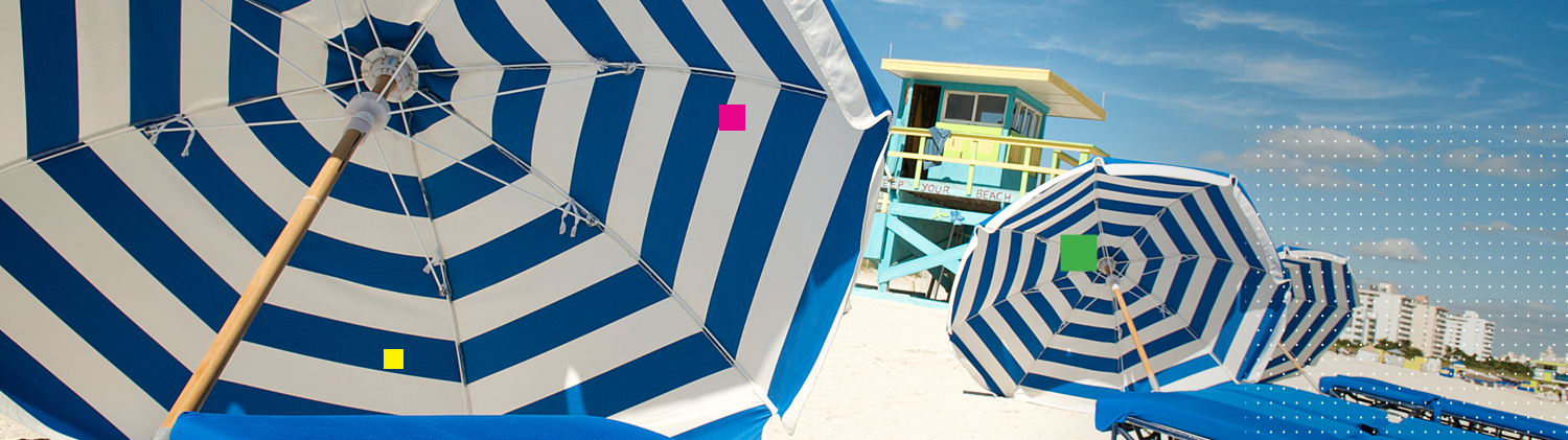 Blue & white striped umbrellas on sand with lifeguard shed in the back