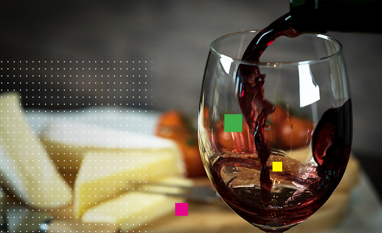 Red wine being poured into glass next to cutting board of cheese