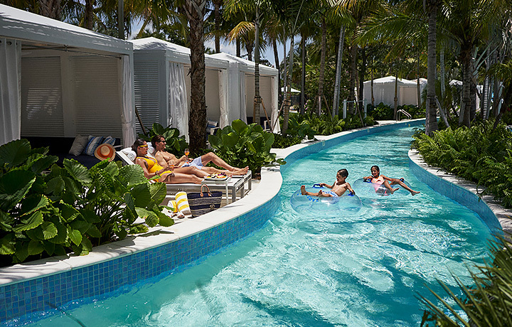childern on a intertube on a lazy river with their parents lounging near the lazy river pool