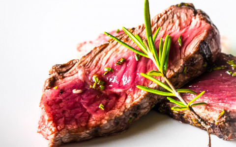Two slices of rare cooked steak with garnish on white background