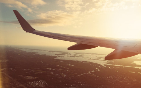 View over plane wing with bright sun burst and coastal landscape below