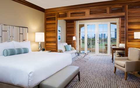 bedroom with white bed and a connected living room that leads to balcony