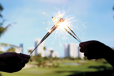 Two Hands Holding Sparklers with a golf course and skyline in the background