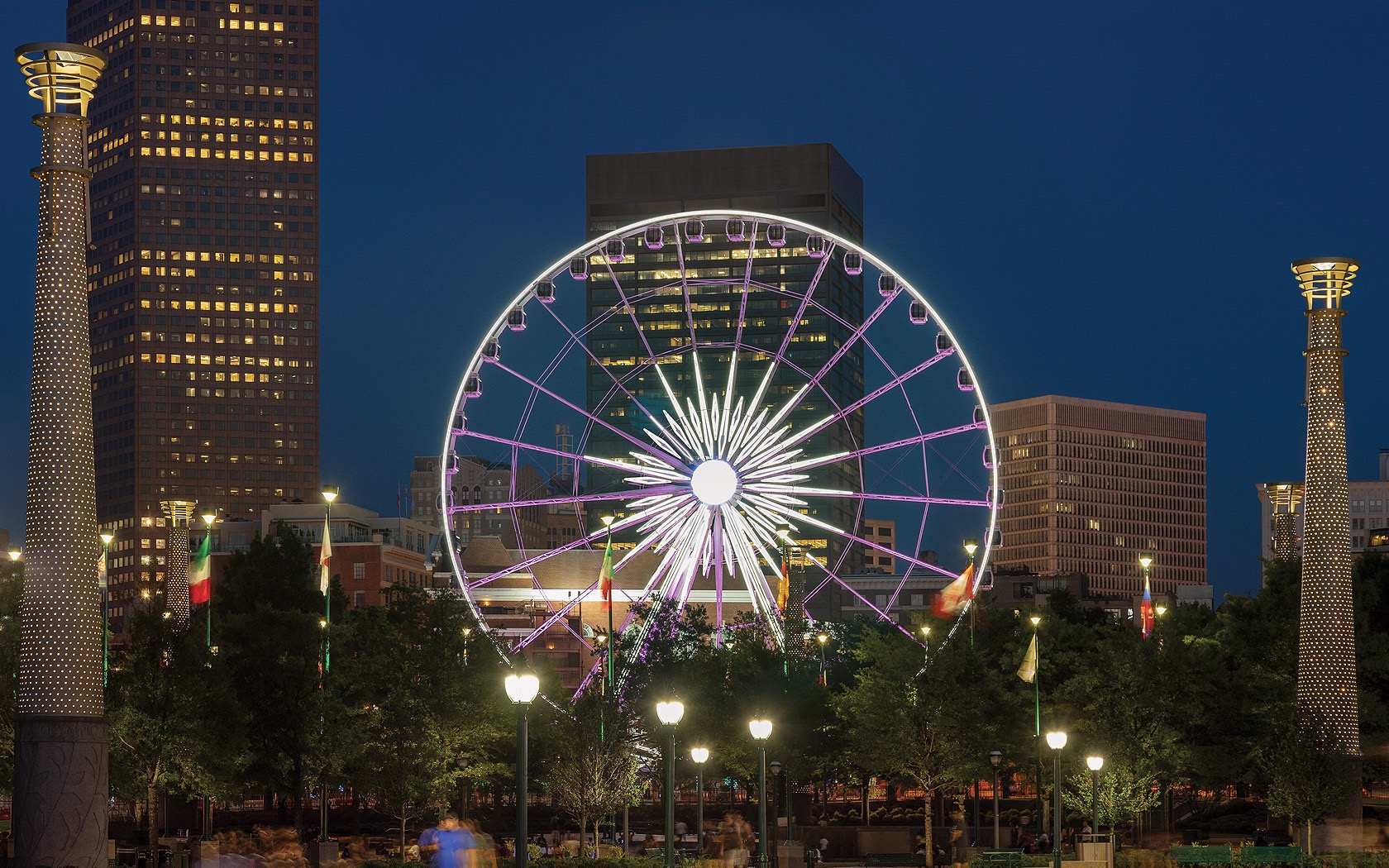 A ferris wheel lit up at night with downtown buildings in the background 