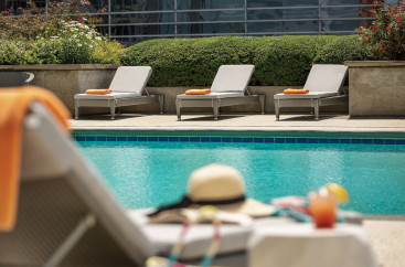A hat sits on a cushioned lounge chair by the pool surrounded by additional lounge chairs 