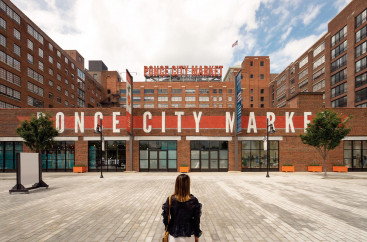 Woman sitting on gray brick ground looking at Ponce City Market sign on a building 