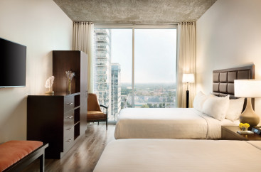 Two beds with a wooden chest and large glass window with a view of downtown 