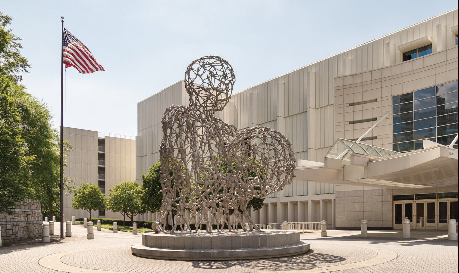 Large wire sculpture of a person holding a ball outside an office building 