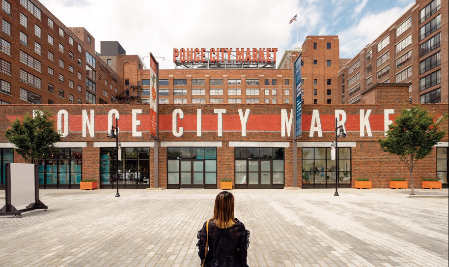 Woman sitting on gray brick ground looking at Ponce City Market sign on a building 