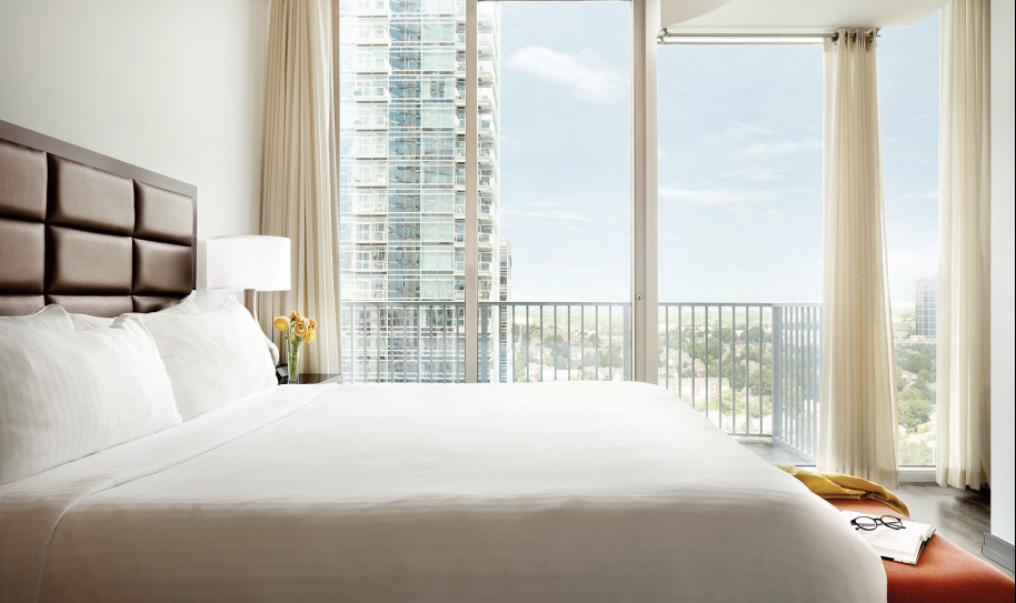 Bed with white sheets and floor length windows facing the city