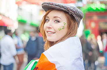 A woman wearing a flat cap with clover stickers on face celebrating St. Patrick's Day