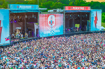 A crowded group of people at an outdoor concert with two stages 