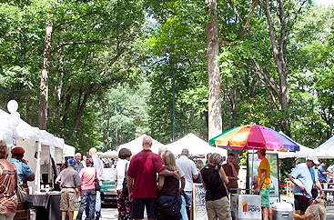 A couple walking into the Chastain Park Art Festival with tents set up in the park