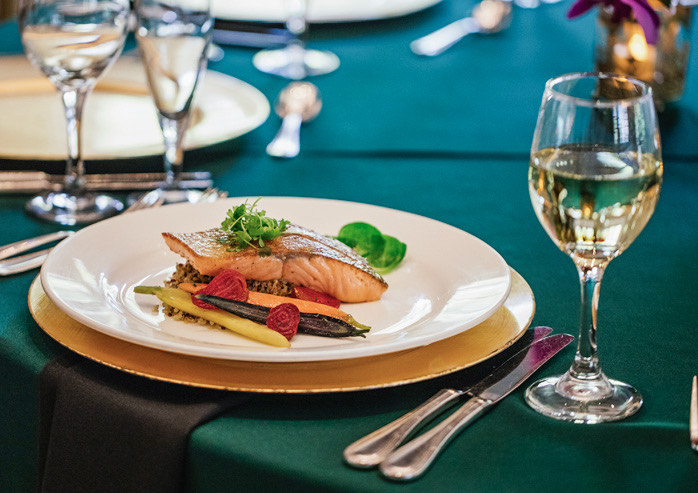 Close up of plated salmon dish on green tablecloth with glass of white wine