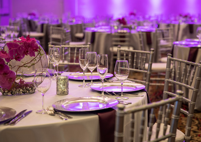 Round table for convention with silver chairs and white table cloth, set up with plate holders and empty wine glasses