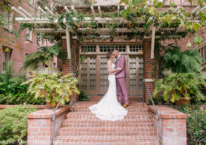 Groom and bride embracing under outdoor canopy surrounded by natural greenery