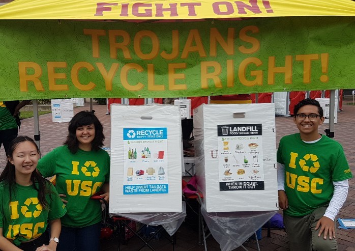 Three Trojan students standing under recycling tent that reads Fight On Trojans Recycle Right