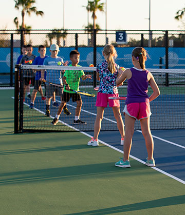 Kids standing in line on court with tennis rackets