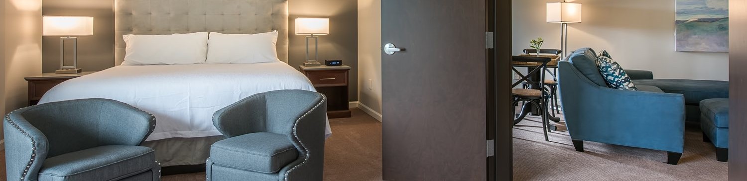 bed with white linens and 2 green chairs