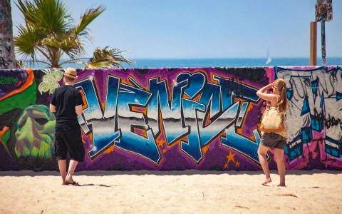 two people standing in front of venice spray painted sign 