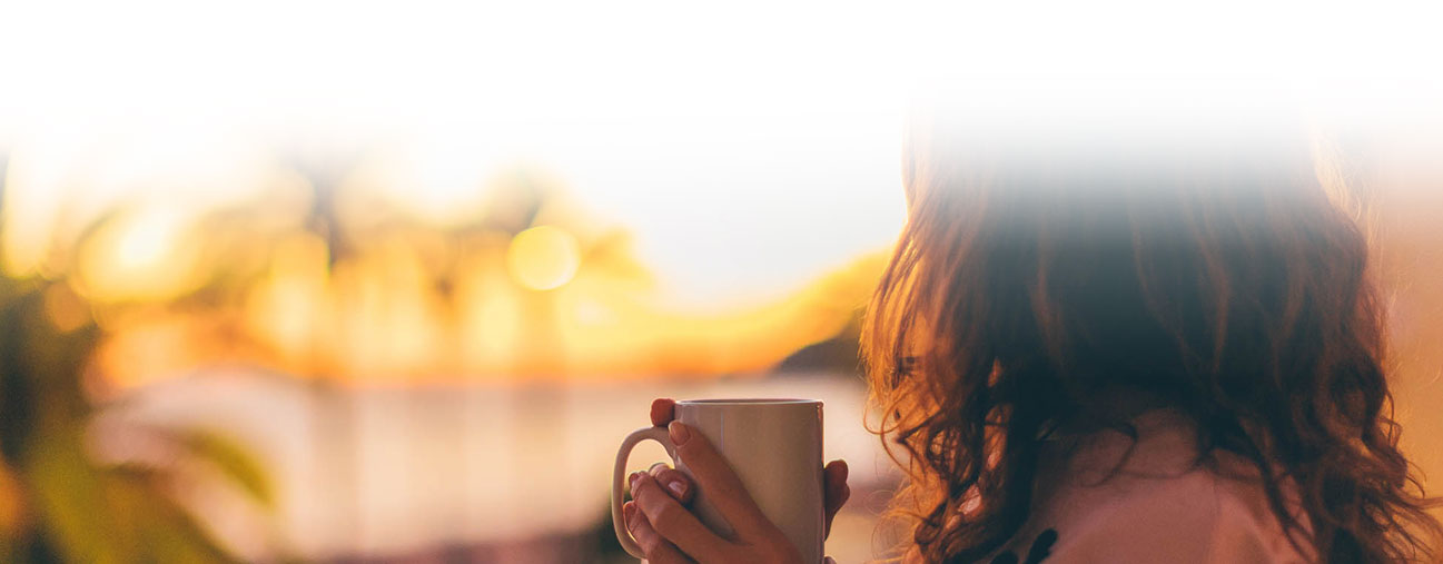 woman enjoying a cup of coffee while watching the sun