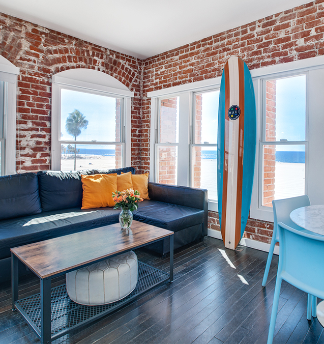 small bedroom with brick wall and surfboard and ocean side view