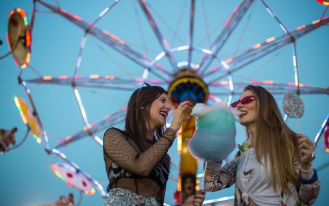 two women eating cotton candy under a ferris wheel 