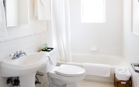 all white bathroom with a bathtub and tile flooring