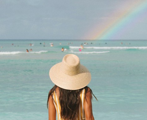 woman with straw hat looking at the rainbow over the ocean