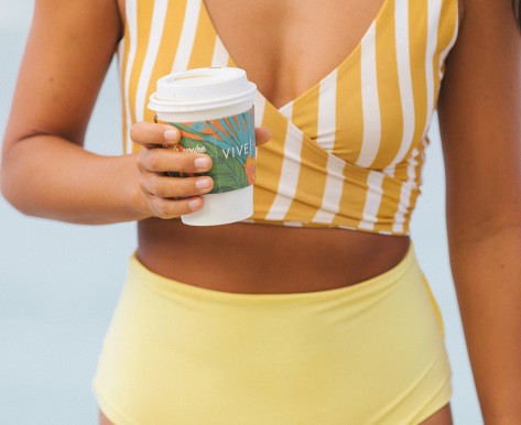 woman in striped yellow bathing suit top and yellow bottoms holding coffee cup