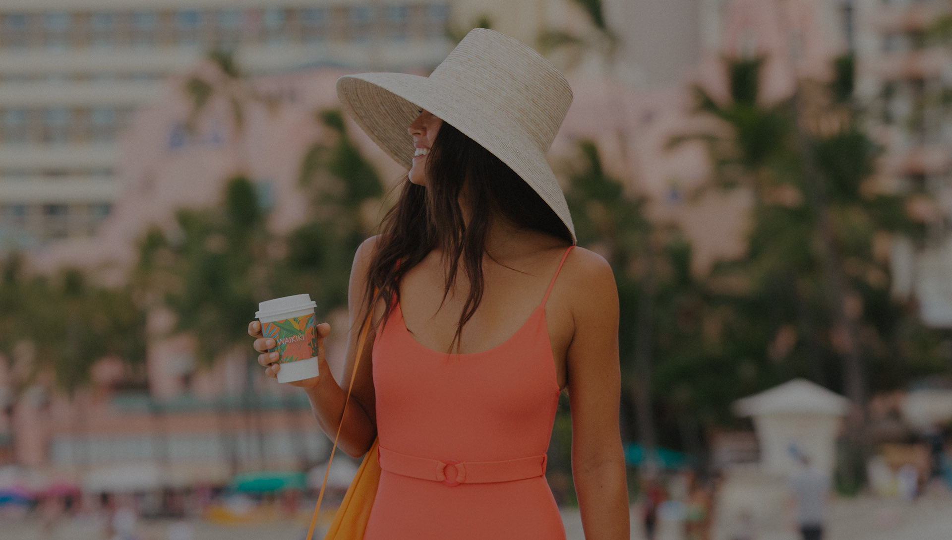 woman in bathing suit with sun hat holding coffee cup