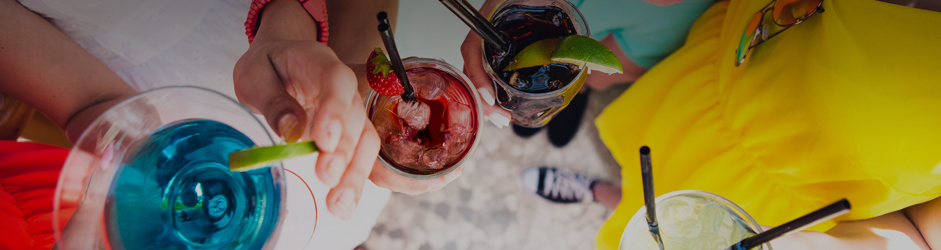 view of hands holding glasses of colorful cocktails