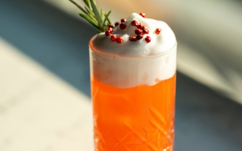 orange cocktail with foam and herbs on top