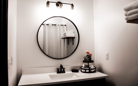 view of a circle mirror on the wall inside a bathroom in black and white tons