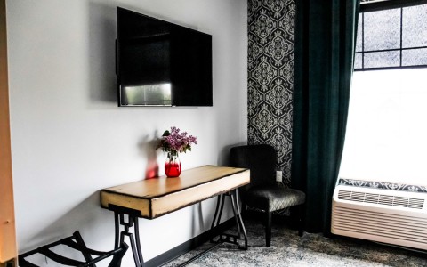 view of a corner hotel room with features as a rectangular desk, small chair and a tv on the wall