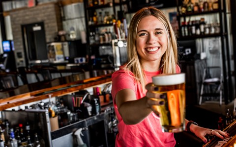 Lady smiling and cheering with a beer at the camera 