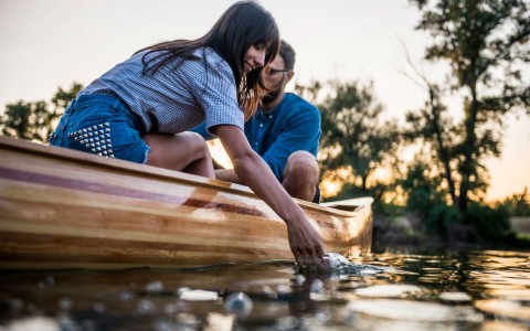Two guys in a canoe while the woman is touching the water