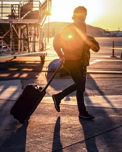 during sunrise a man carrying a jacket pushing his suitcase