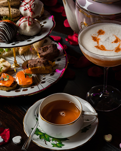 Tea cup and tray with assorted tea sandwiches, pastries, and a cocktail in a coupe glass