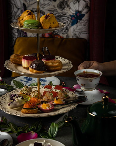 Tea tower with spring pastries and tea sandwiches, tea pot and hand holding tea cup filled with tea