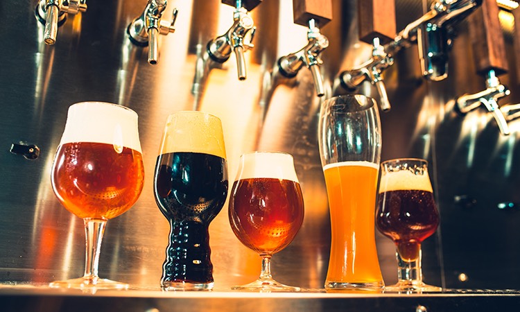 beer glasses of various shapes and colors sitting underneath beer taps